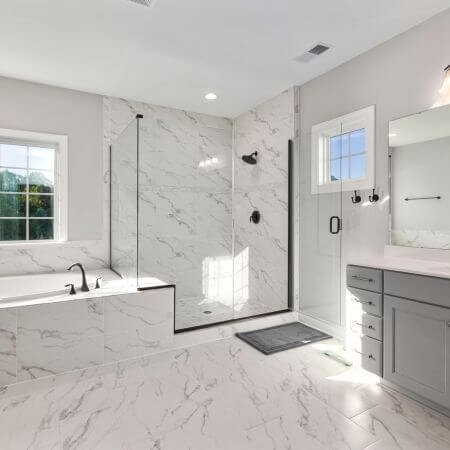 A modern bathroom with a white bathtub, sink, and toilet. The walls are tiled in light gray with a large mirror above the sink.