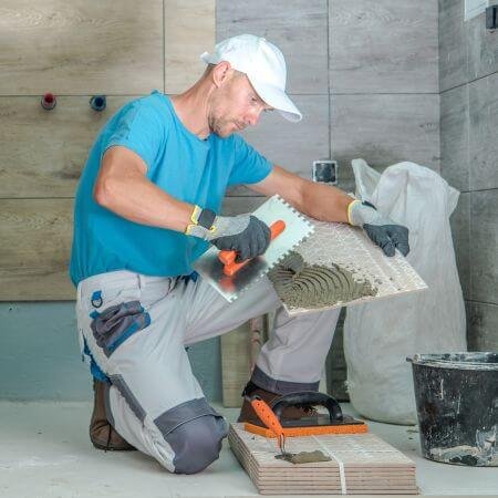 A man is laying tiles on a bathroom floor, carefully working to create a beautiful and functional space.