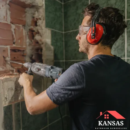 A contractor wearing safety gear uses a rotary hammer for bathroom demolition.