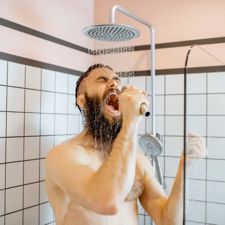 A man singing into a microphone in a modern shower.