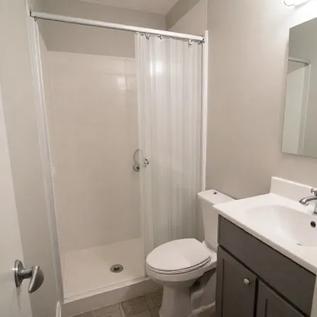 A small remodeled bathroom with a white shower stall, toilet, and vanity.